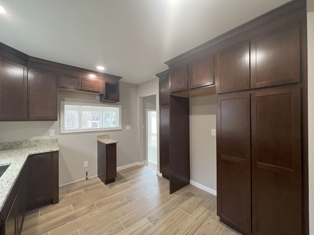 kitchen with wood tiled floor, dark brown cabinetry, baseboards, and light stone countertops