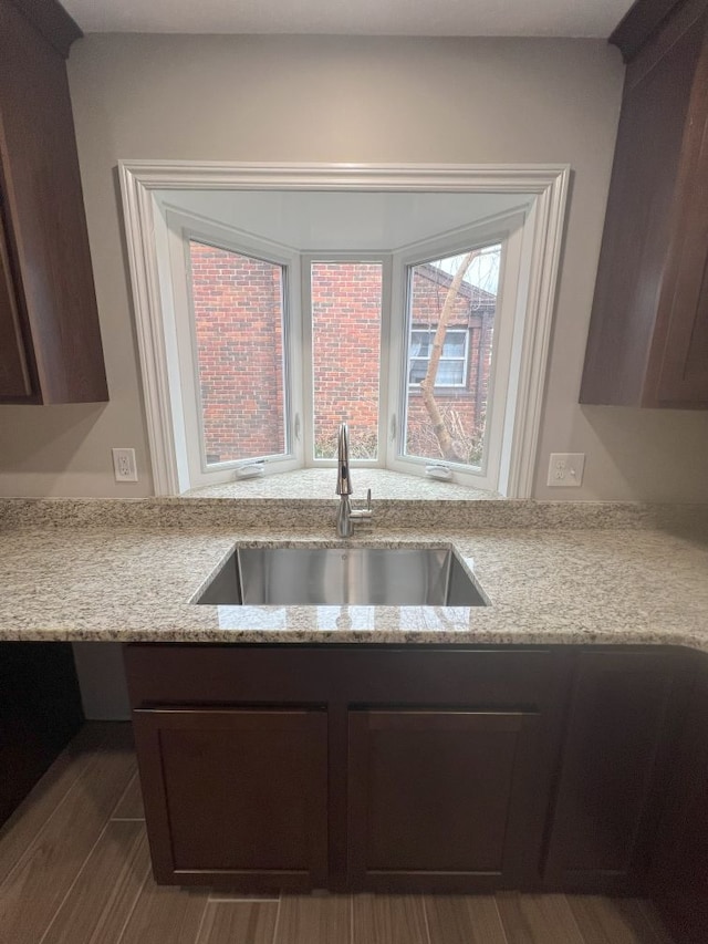 kitchen with a sink, dark brown cabinetry, and light stone countertops