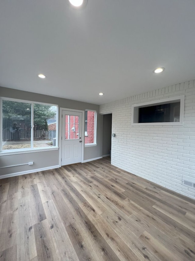 unfurnished living room featuring recessed lighting, baseboards, brick wall, and wood finished floors