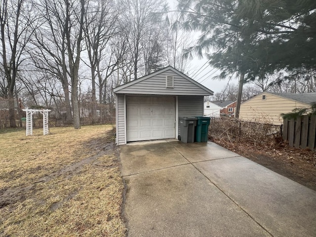 detached garage featuring concrete driveway and fence