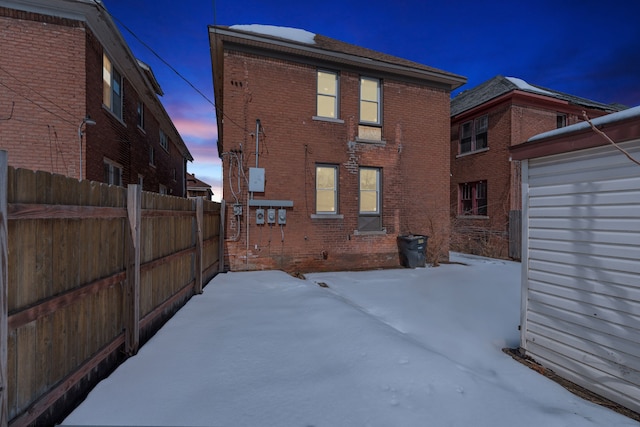 snow covered property with brick siding and fence