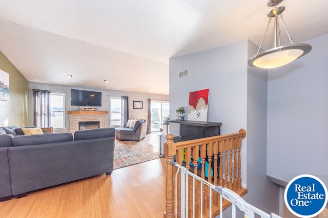 living room featuring light wood finished floors, a brick fireplace, visible vents, and a healthy amount of sunlight