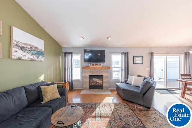 living room featuring vaulted ceiling, a fireplace, light wood-style flooring, and baseboards