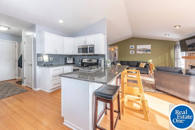 kitchen featuring stainless steel appliances, open floor plan, white cabinets, and a breakfast bar area