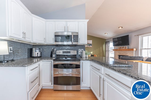 kitchen featuring vaulted ceiling, stainless steel appliances, dark stone counters, and white cabinetry