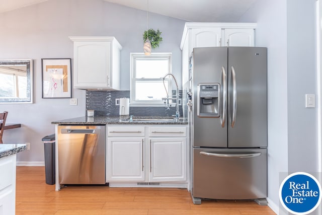 kitchen featuring light wood finished floors, stainless steel appliances, decorative backsplash, white cabinets, and dark stone countertops