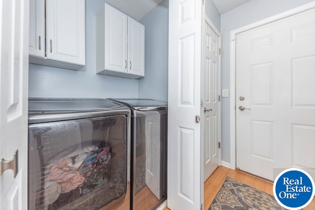 laundry room with washing machine and clothes dryer, cabinet space, and light wood-style floors