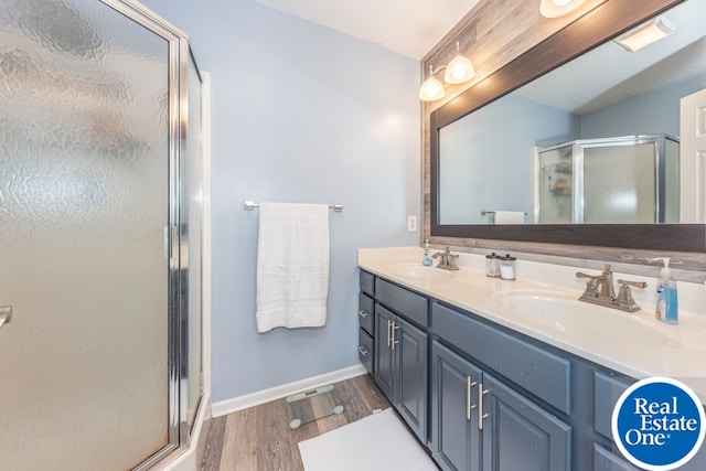 full bath featuring a stall shower, double vanity, a sink, and wood finished floors