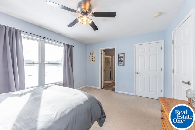 bedroom featuring baseboards, ensuite bathroom, a ceiling fan, and light colored carpet