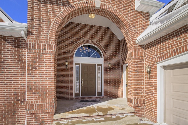 view of exterior entry featuring a garage and brick siding