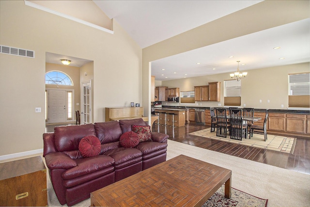 living area with a chandelier, high vaulted ceiling, dark wood-type flooring, visible vents, and baseboards