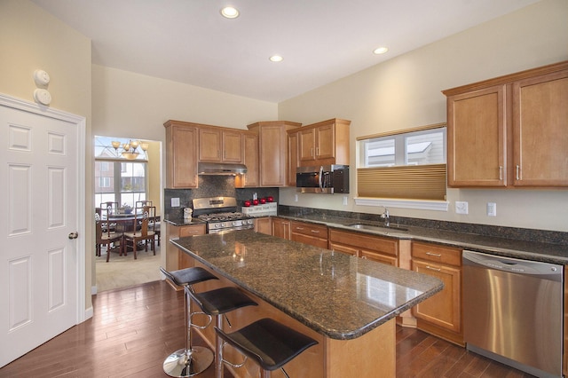 kitchen featuring a center island, appliances with stainless steel finishes, a sink, under cabinet range hood, and a kitchen bar