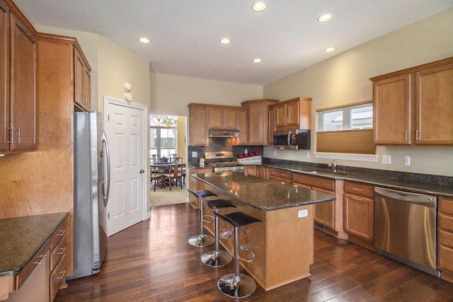 kitchen with appliances with stainless steel finishes, brown cabinetry, a kitchen island, and under cabinet range hood