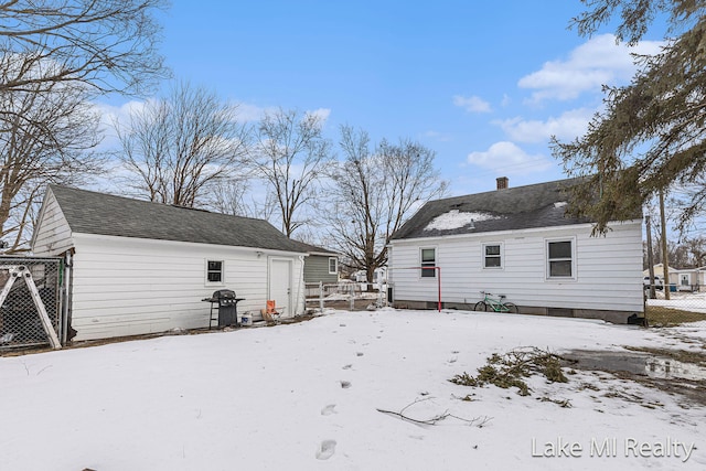 snow covered back of property featuring a chimney and fence