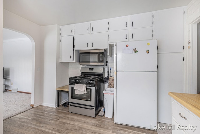 kitchen with arched walkways, white cabinetry, light countertops, appliances with stainless steel finishes, and light wood finished floors