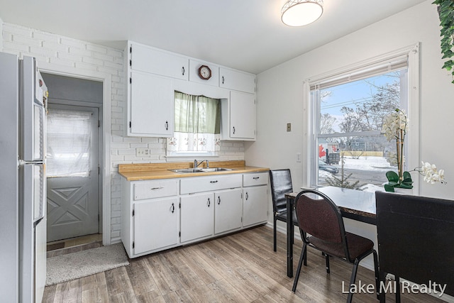 kitchen featuring tasteful backsplash, light wood-style flooring, freestanding refrigerator, white cabinets, and a sink