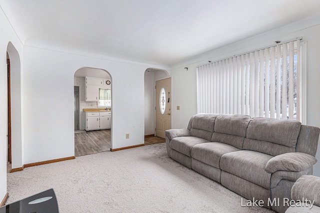 living room with arched walkways, carpet floors, and baseboards