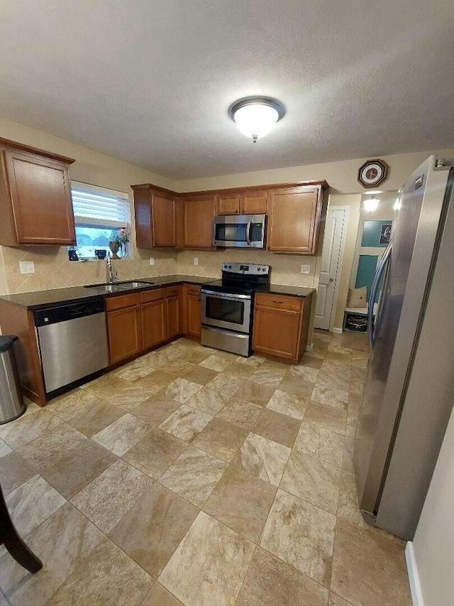 kitchen with brown cabinets, dark countertops, backsplash, appliances with stainless steel finishes, and a sink