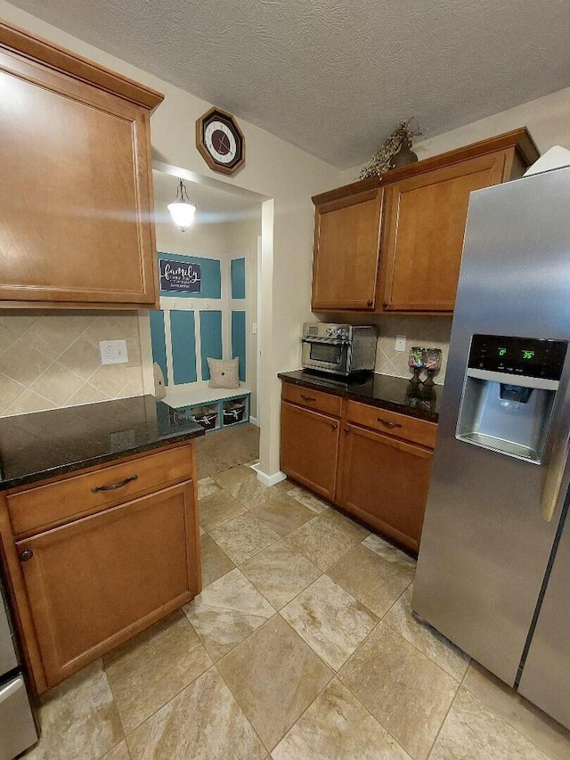 kitchen featuring tasteful backsplash, stainless steel fridge, a toaster, dark stone counters, and brown cabinetry