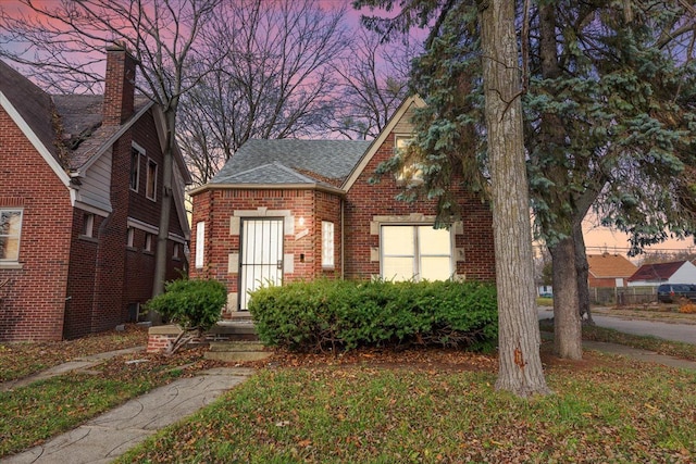 view of front facade with a front yard, brick siding, and roof with shingles