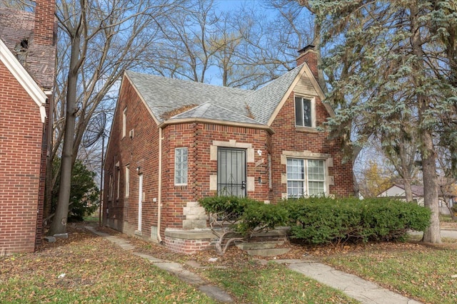 tudor-style house with a shingled roof, a chimney, and brick siding