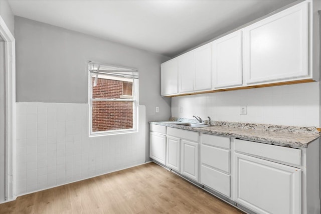 kitchen with light wood-style floors, tile walls, white cabinetry, and a sink