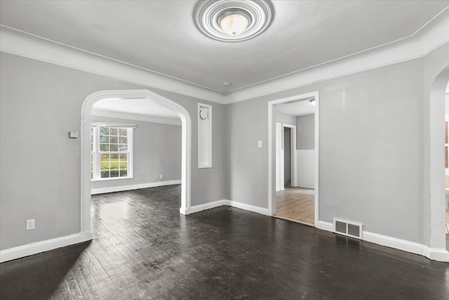 unfurnished room with visible vents, arched walkways, dark wood finished floors, and baseboards