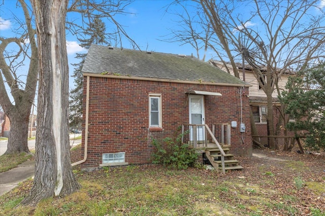 rear view of house featuring brick siding and roof with shingles