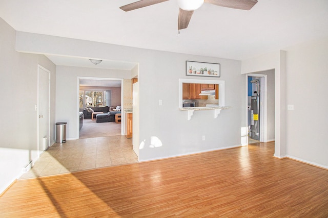 unfurnished living room with a ceiling fan, light wood-type flooring, gas water heater, and baseboards