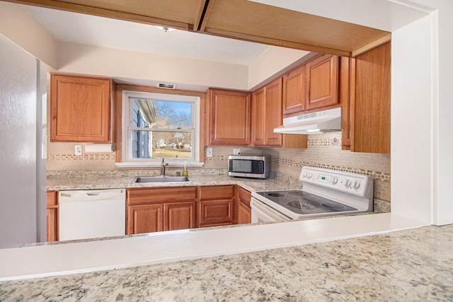 kitchen with white appliances, tasteful backsplash, under cabinet range hood, and a sink