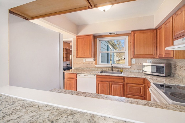 kitchen featuring under cabinet range hood, white appliances, a sink, backsplash, and brown cabinets