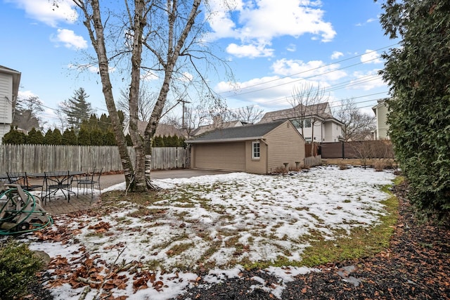 snowy yard featuring a garage, an outdoor structure, and a fenced backyard