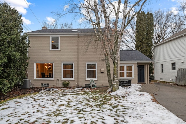 view of front of property featuring a chimney, central AC unit, and brick siding