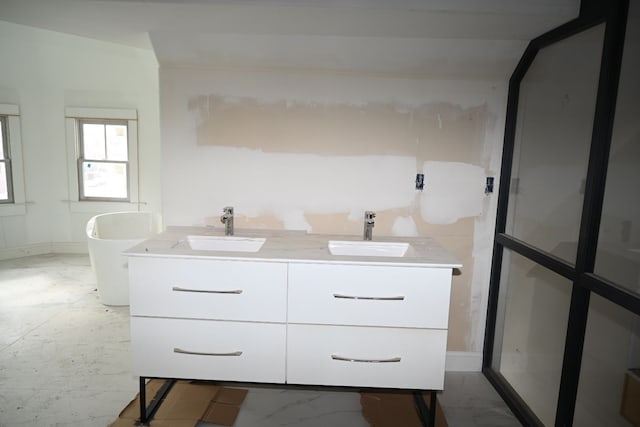 bathroom with a freestanding tub, marble finish floor, a sink, and double vanity