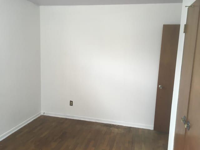 unfurnished room featuring baseboards and dark wood-type flooring