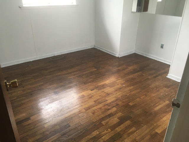 spare room featuring dark wood-type flooring, visible vents, and baseboards