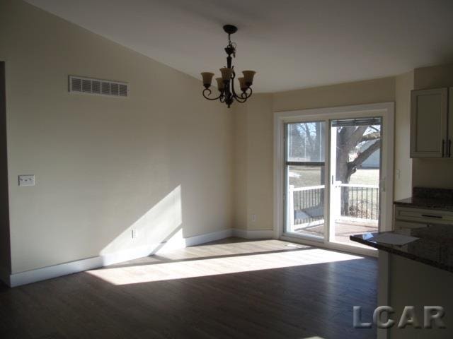 unfurnished dining area featuring baseboards, visible vents, lofted ceiling, wood finished floors, and an inviting chandelier