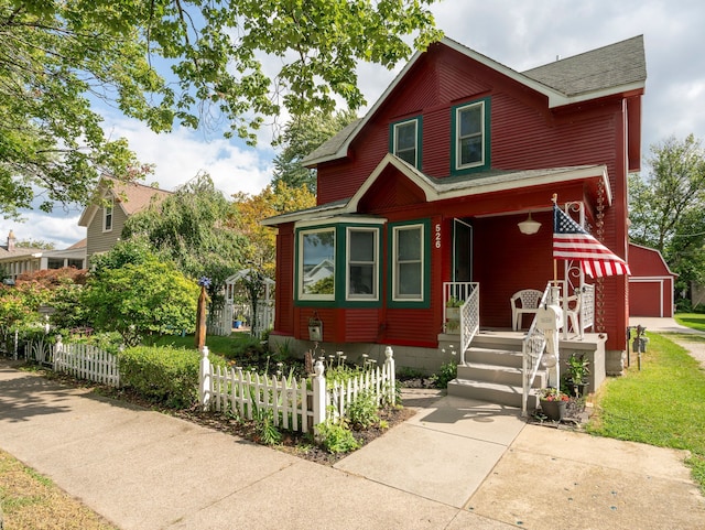 view of front facade with a fenced front yard, an outbuilding, a shingled roof, and a detached garage