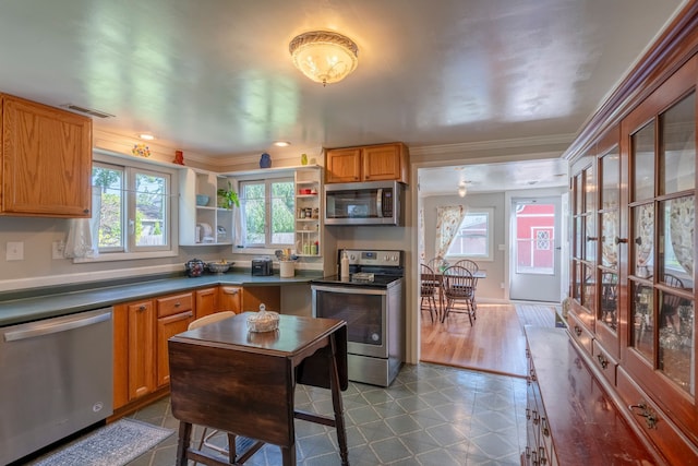 kitchen with appliances with stainless steel finishes, dark countertops, brown cabinets, and ornamental molding