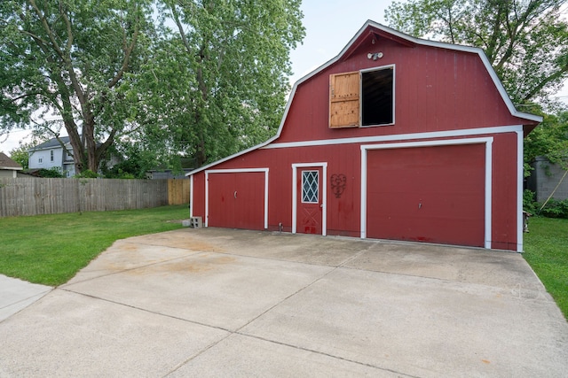 view of barn featuring concrete driveway, fence, and a lawn