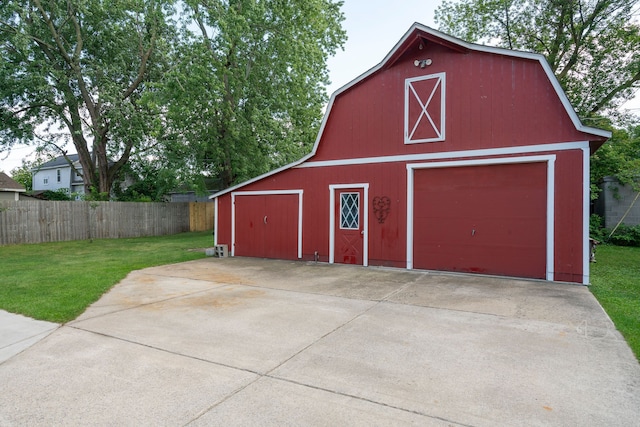 view of barn with fence, driveway, and a lawn