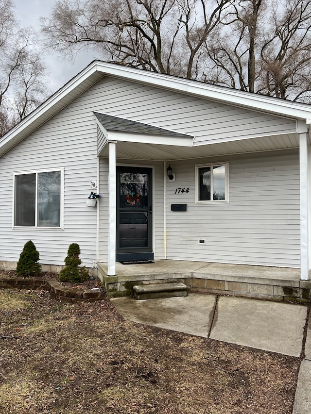 entrance to property featuring a shingled roof and a porch