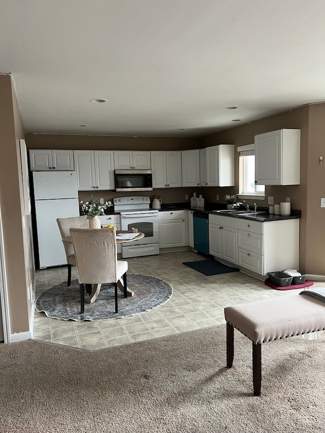 kitchen with dark countertops, white appliances, white cabinetry, and a sink