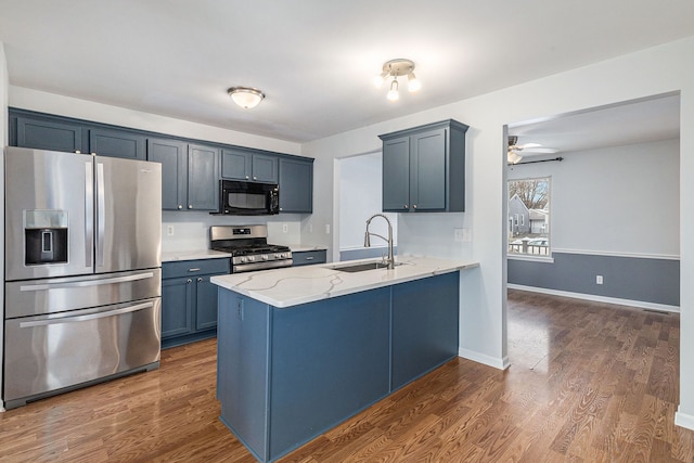 kitchen featuring dark wood finished floors, appliances with stainless steel finishes, a sink, light stone countertops, and a peninsula