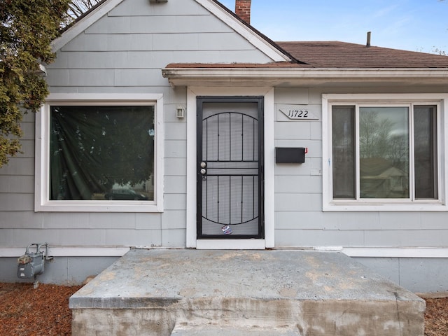 doorway to property with a chimney and a shingled roof