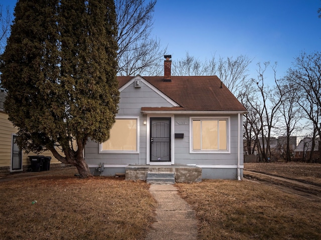 bungalow featuring a front lawn, a chimney, and a shingled roof