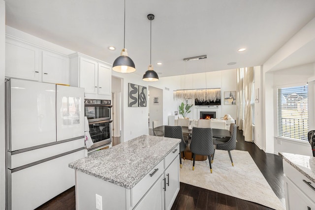 kitchen featuring light stone counters, dark wood finished floors, freestanding refrigerator, open floor plan, and white cabinets