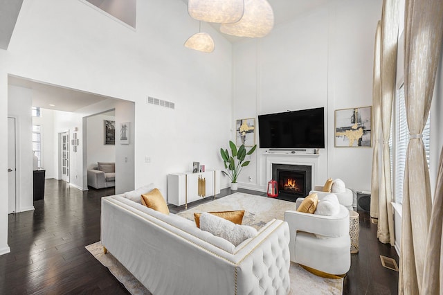 living area featuring a towering ceiling, wood finished floors, a fireplace with flush hearth, and visible vents