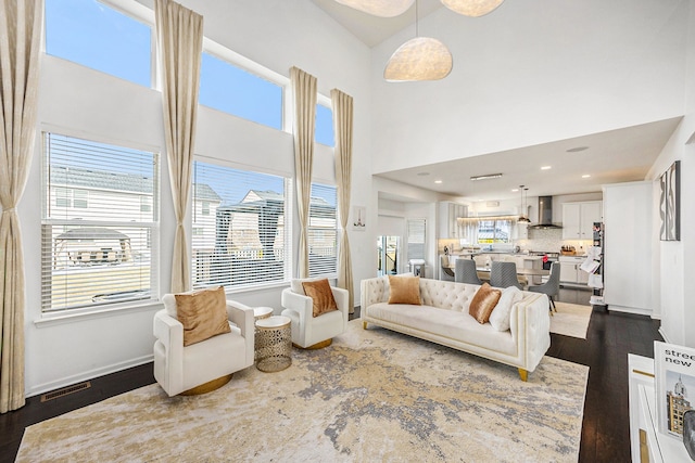 living area featuring a towering ceiling, dark wood-style floors, baseboards, and visible vents