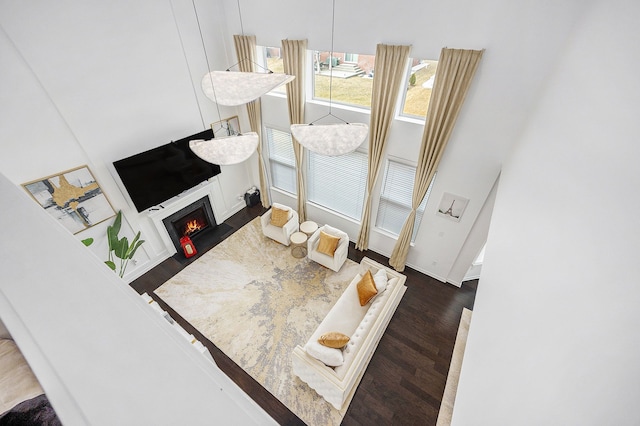 living area with dark wood-style flooring, a lit fireplace, and baseboards